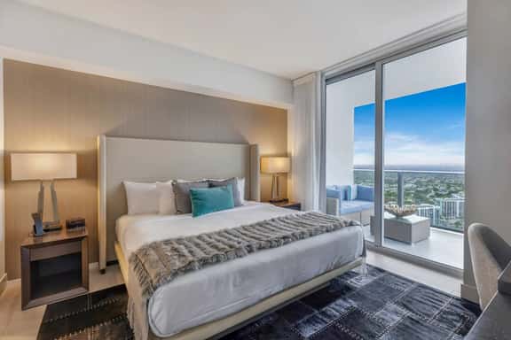 Step into the second bedroom, where a king-size bed, elegant lighting, and cozy design set the scene. An in-room bathroom and dedicated workspace add convenience, while sliding doors open to a balcony with sweeping city and ocean views.