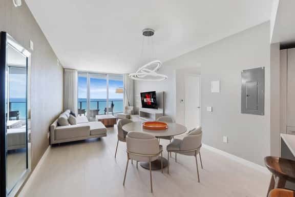 The dining area sits at the center of the open layout, offering a stylish round table and a bright setting for meals with an ocean backdrop.