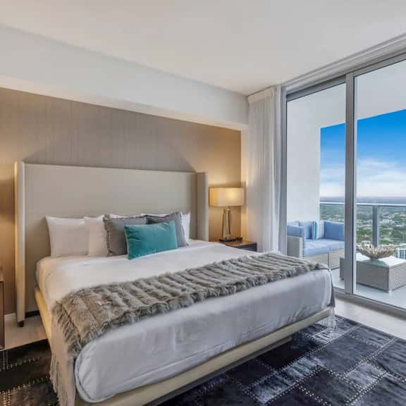 Step into the second bedroom, where a king-size bed, elegant lighting, and cozy design set the scene. An in-room bathroom and dedicated workspace add convenience, while sliding doors open to a balcony with sweeping city and ocean views.