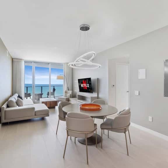 The dining area sits at the center of the open layout, offering a stylish round table and a bright setting for meals with an ocean backdrop.