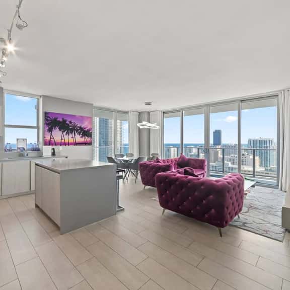 Enjoy an open-plan living space with a sleek kitchen and dining area. Large windows fill the room with natural light and offer expansive city and ocean views, creating a bright and inviting atmosphere for your stay.